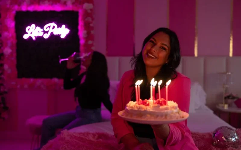 A woman celebrating her birthday with cake and candles in a vibrant pink-themed party setting.