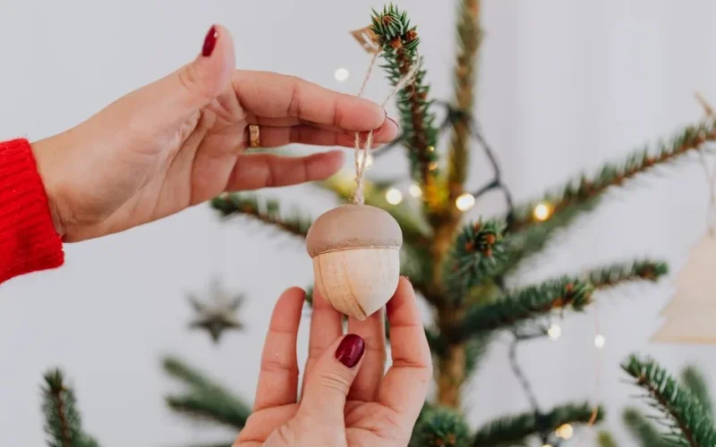 Close-up of hands hanging an acorn ornament on a decorated Christmas tree.