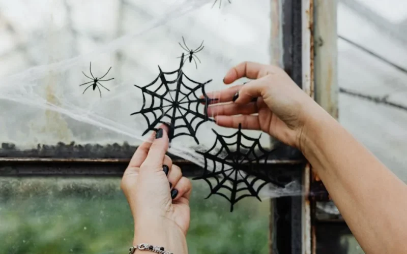 Hands decorating a window with spider web crafts for Halloween, capturing a spooky seasonal vibe.