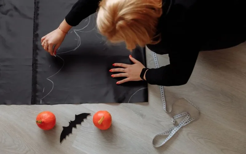 A woman crafting a Halloween costume indoors with pumpkins and fabric.