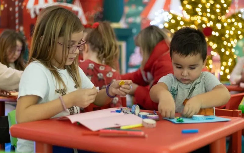 Kids creating festive crafts in a colorful, Christmas-themed classroom setting, focused on holiday creativity.