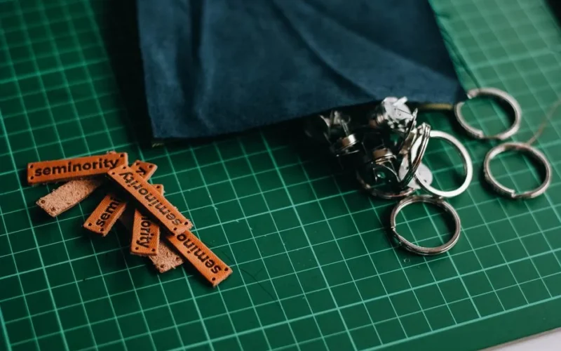 Close-up of leather tags labeled 'seminority' and metal rings on a green cutting mat, ideal for crafting themes.