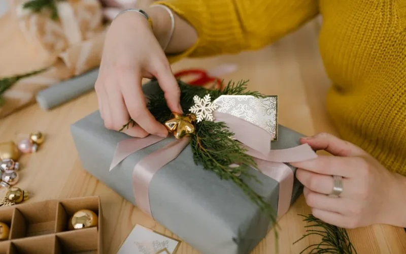 Close-up of hands wrapping a Christmas gift with ribbon and festive decorations.