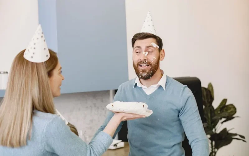 Man and woman sharing a playful cake smash during a birthday celebration indoors.