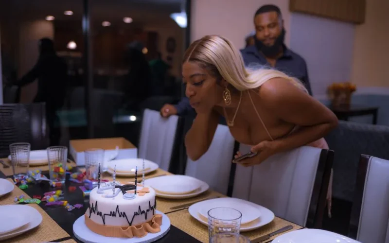 Woman blowing out candles on a decorated birthday cake at a stylish party setting.