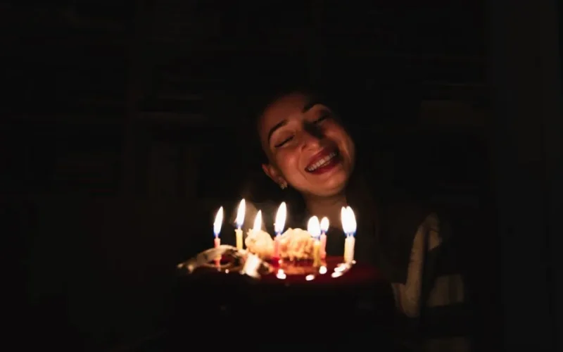 A joyful woman smiles at a cake lit with candles during her birthday celebration.