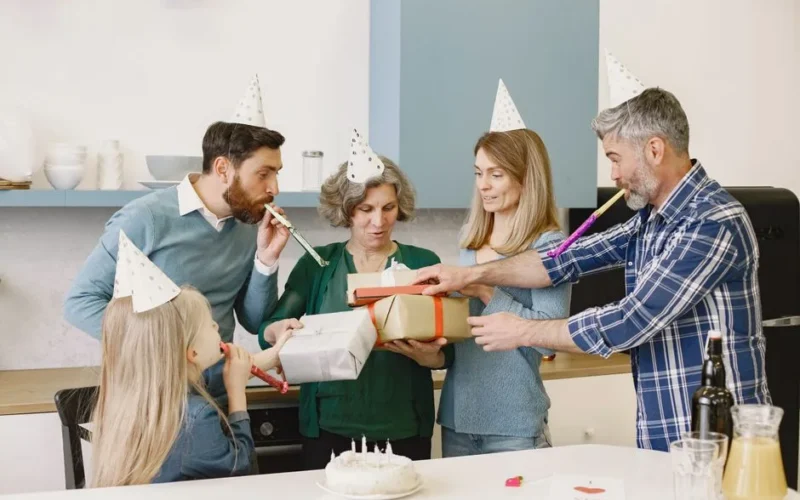 Happy family celebrating with party hats, gifts, and a cake indoors.