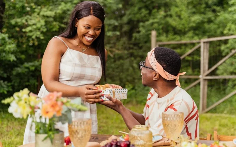 A joyful moment of gift exchange between friends at an outdoor summer gathering.