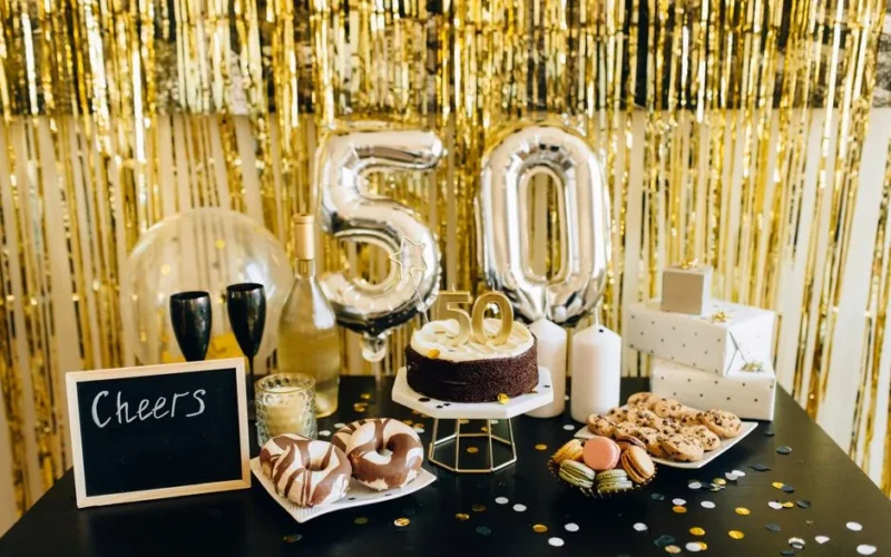 Stylish 50th birthday party setup with cake, balloons, gifts, and champagne amidst golden decorations.