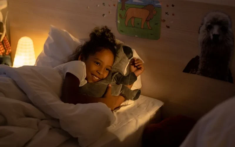 Young girl cuddles with her stuffed toy in a warmly lit bedroom, creating a serene bedtime atmosphere.