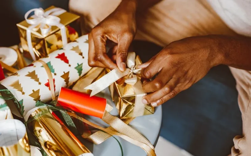 Hands tying ribbons on Christmas gifts with festive wrapping paper and gold accents.