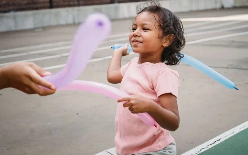 Smiling child playing with colorful balloons outdoors in a playground.