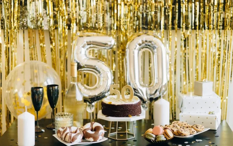 Stylish 50th birthday party setup with cake, gifts, and balloons in gold theme.