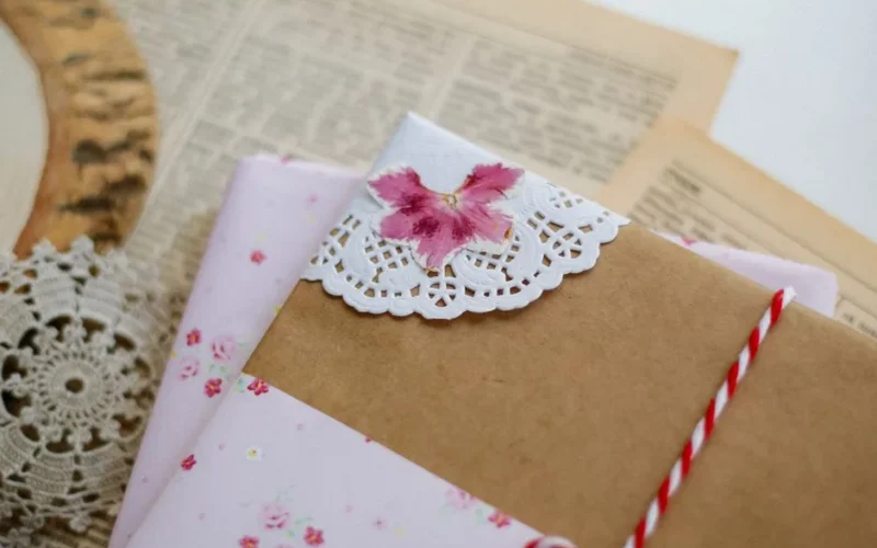 A beautifully wrapped handmade gift with floral accents and a decorative paper doily on antique paper.