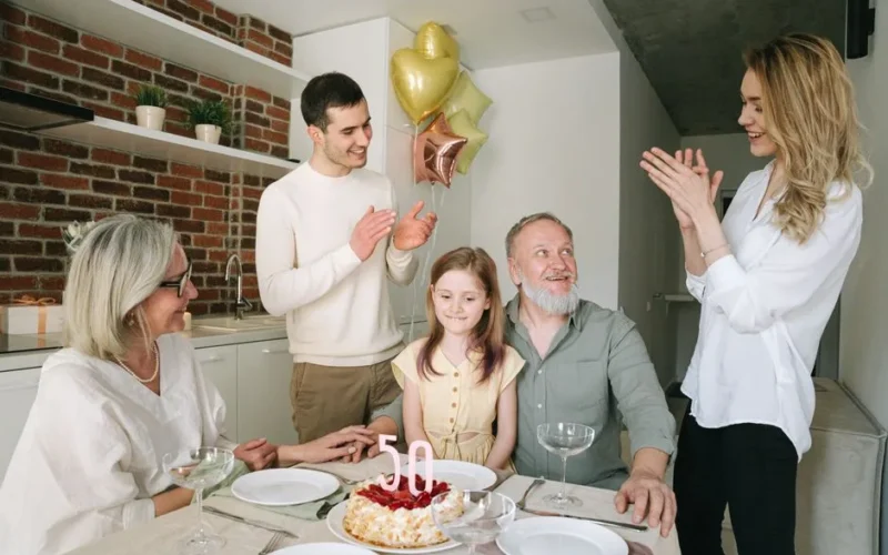 Happy family celebrating a 50th birthday with cake and balloons, enjoying togetherness indoors.