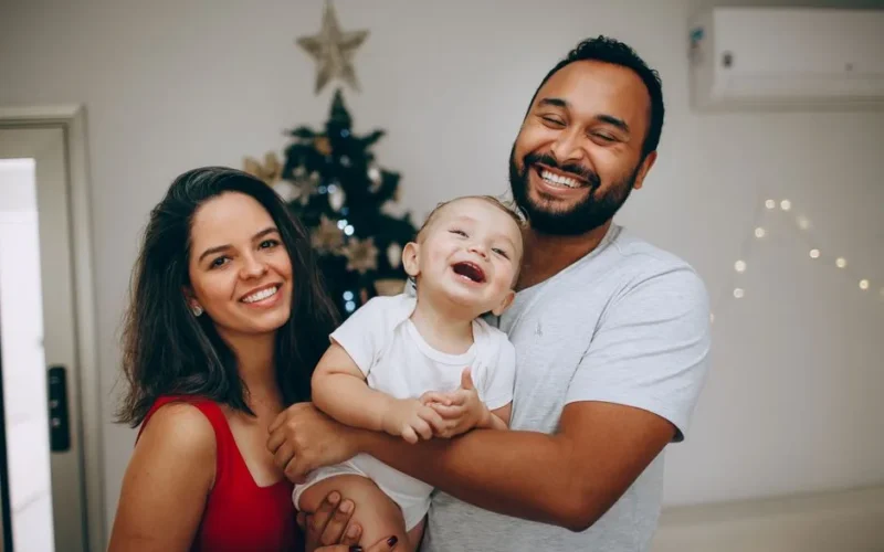 Smiling family enjoying festive Christmas moments indoors with a decorated tree.