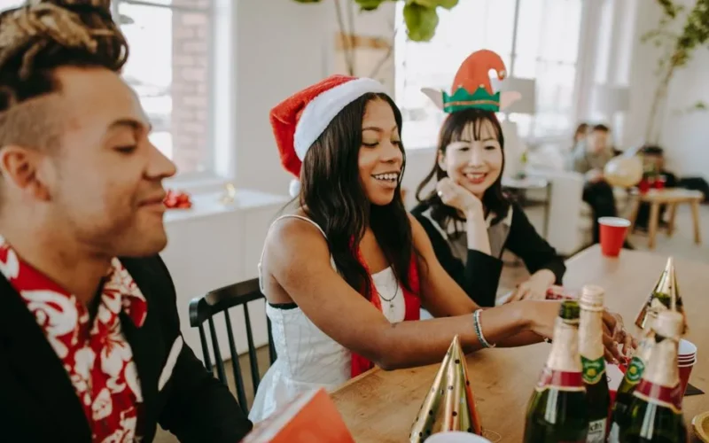 Diverse coworkers enjoying a joyful Christmas office party with drinks and festive hats.