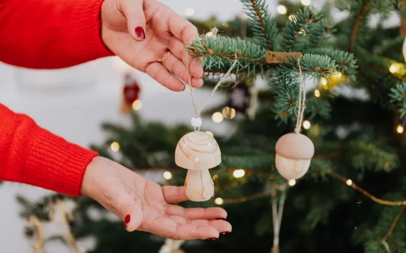 Hands decorating a Christmas tree with wooden mushroom ornaments, adding a rustic charm.
