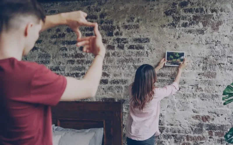 Couple arranging a photo on a rustic brick wall, adding artistic decor to their home.
