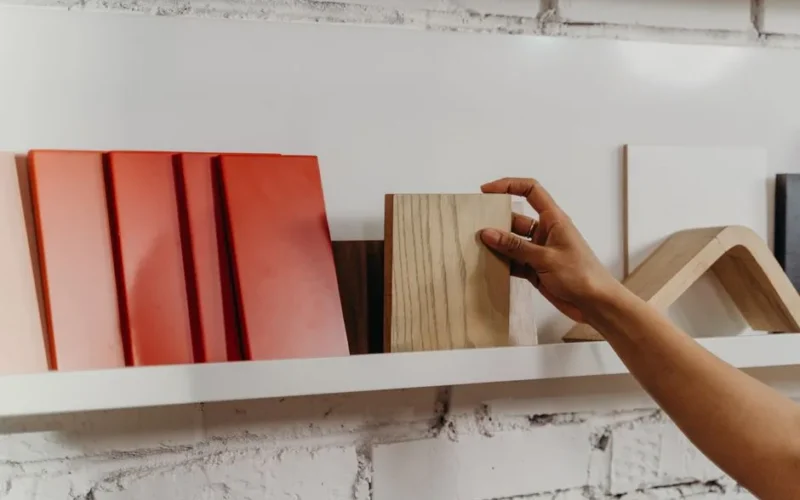 A hand selecting a wooden sample from a display shelf featuring various construction materials.