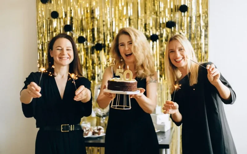 Happy women celebrating a 50th birthday with cake and sparklers indoors.