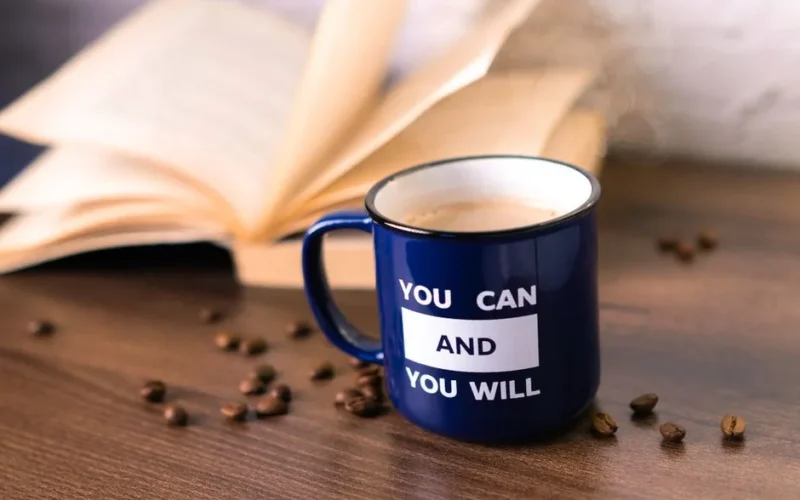 Inspirational coffee moment with a motivational quote on a mug beside an open book.
