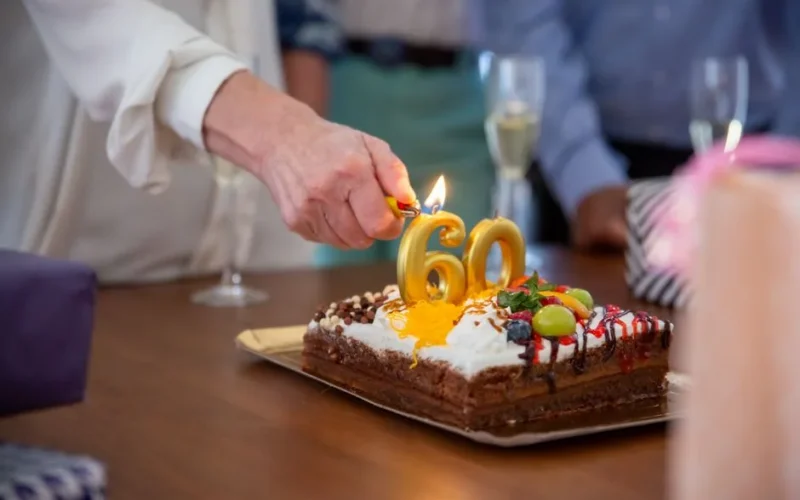 Hand lighting candles on birthday cake with number 60 on it at a celebration.