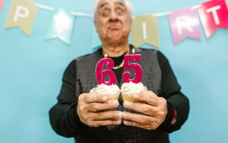Senior man holding cupcakes with 65 candle during his birthday celebration.
