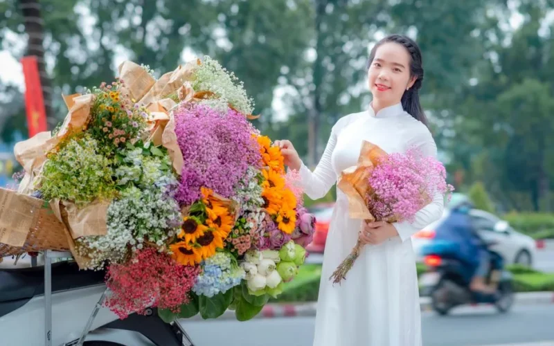 A woman in a white dress happily holding a bouquet of vibrant flowers outdoors.
