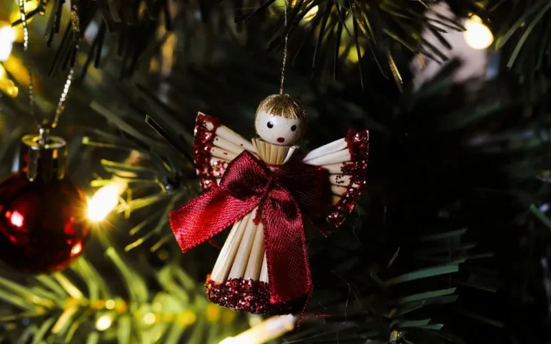 Close-up of a handmade Christmas angel ornament hanging on a festive tree branch.