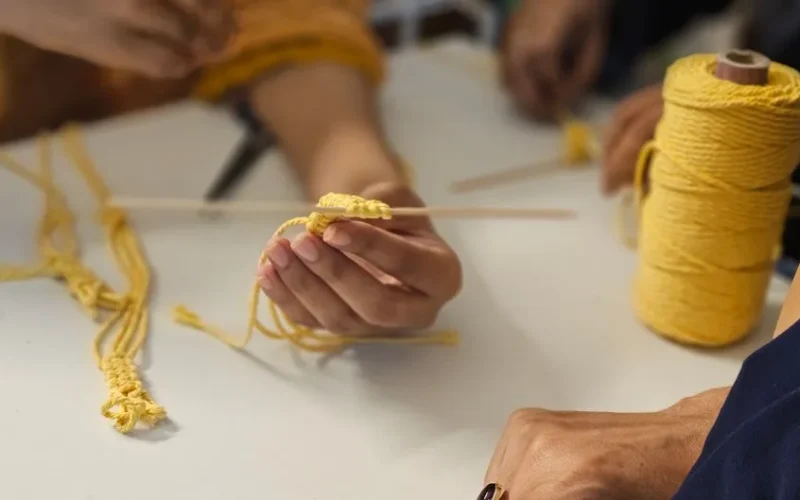 A detailed view of hands creating a handmade craft using yellow yarn and a tool.