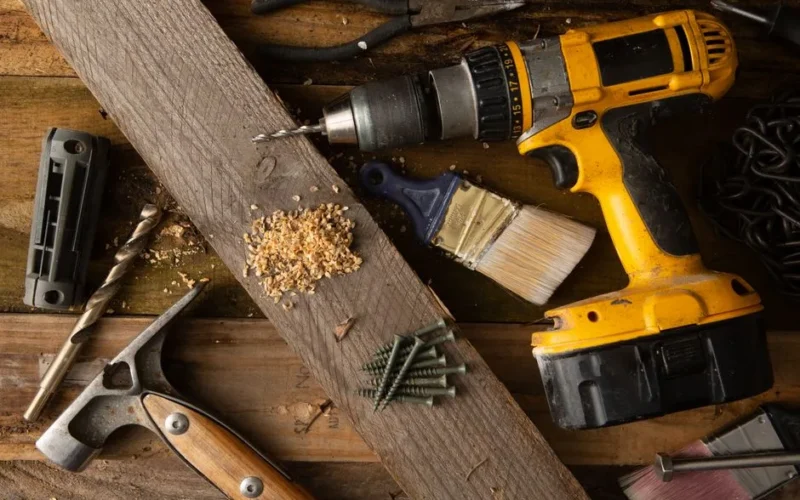 A close-up of various tools including a drill, hammer, and paintbrush on a wooden workbench.