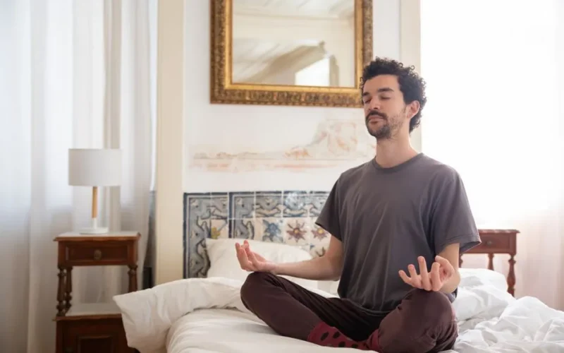 Discover tranquility as a man meditates in a serene bedroom environment, capturing the essence of peace.