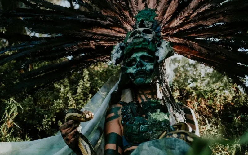 A mystical character with elaborate headgear and snake amidst lush greenery.