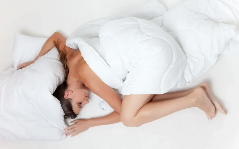A serene image of a woman sleeping comfortably wrapped in a white duvet on a plain bed.