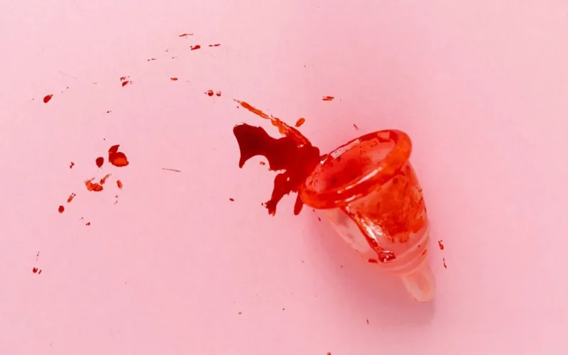 A menstrual cup with spilled blood on a pink surface, symbolizing menstruation and women's health.