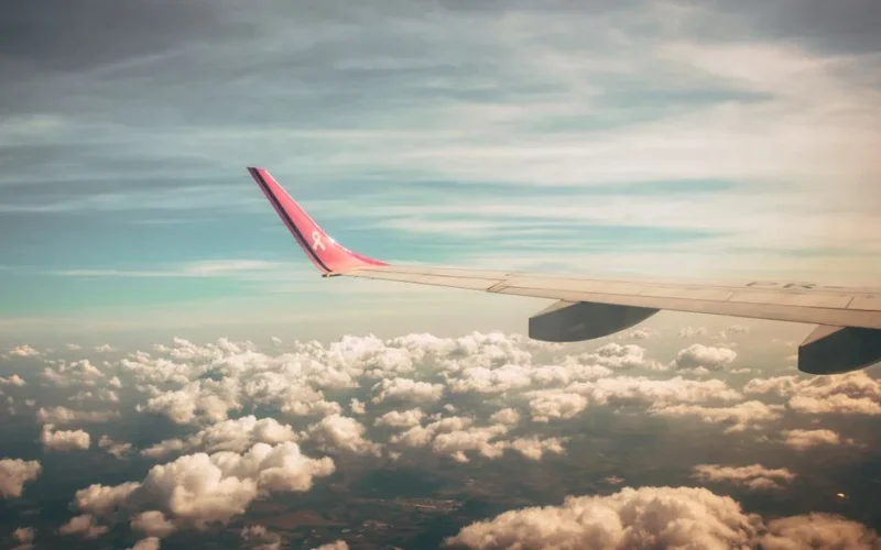 A picturesque view from an airplane window, capturing the wing against a backdrop of fluffy clouds and a vibrant sky at dawn.
