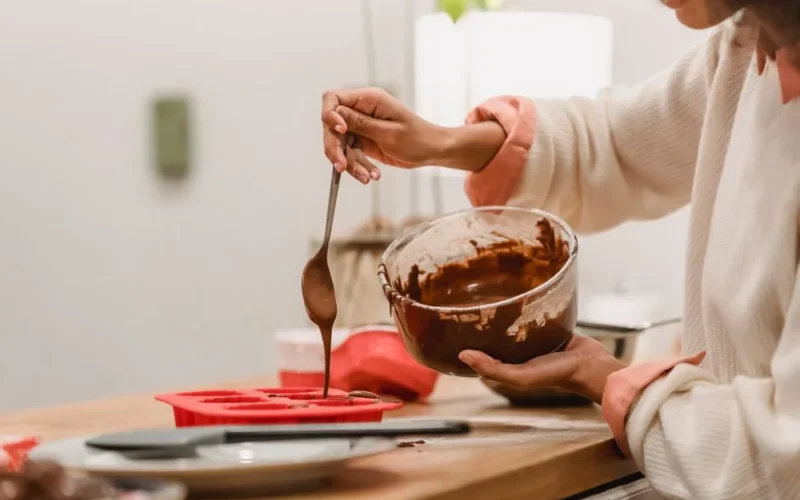 Crop anonymous African American female pouring sweet tasty melted chocolate in red silicone baking dish