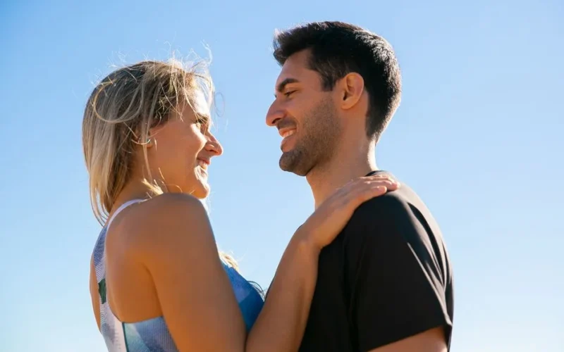 A joyful couple smiling at each other beneath a clear blue sky, symbolizing love and happiness.