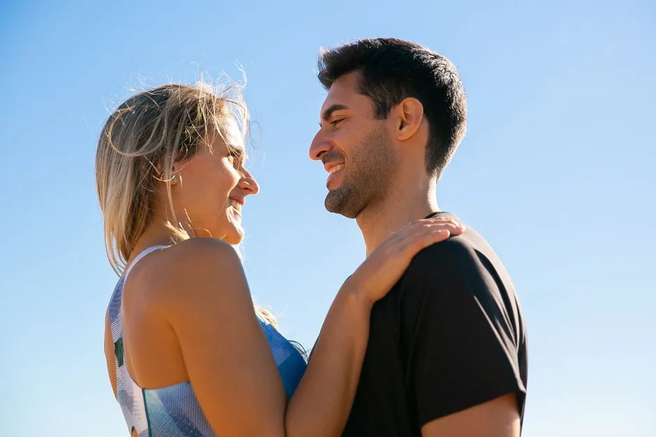 A joyful couple smiling at each other beneath a clear blue sky, symbolizing love and happiness.