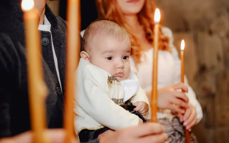 A peaceful Orthodox baptism scene with a baby held by family members holding candles.