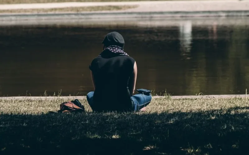 A woman sits by a river enjoying the peaceful outdoors under a tree.