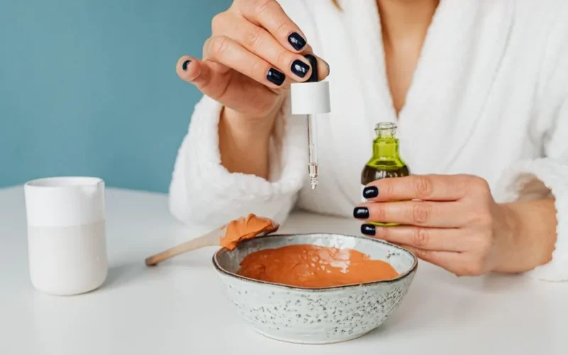 A woman in a bathrobe mixing ingredients for a DIY skincare mask using a pipette.