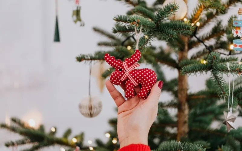 Hand decorating Christmas tree with red polka dot ornament, creating a festive holiday atmosphere.