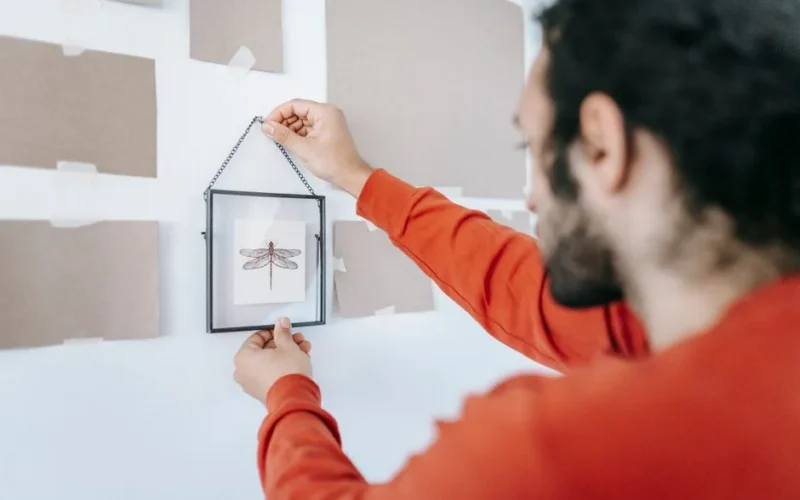 A man hangs a picture frame on the wall while decorating a modern, minimalist home interior.