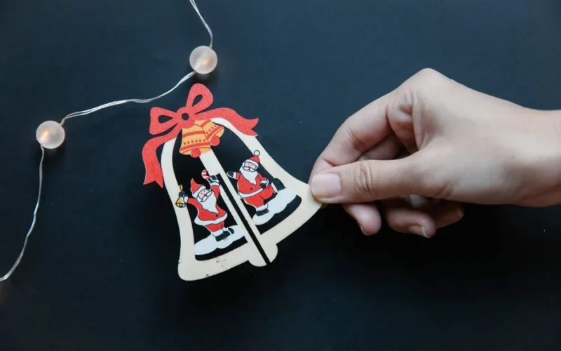 From above of unrecognizable woman holding little cute carton Christmas bell while making handmade garland