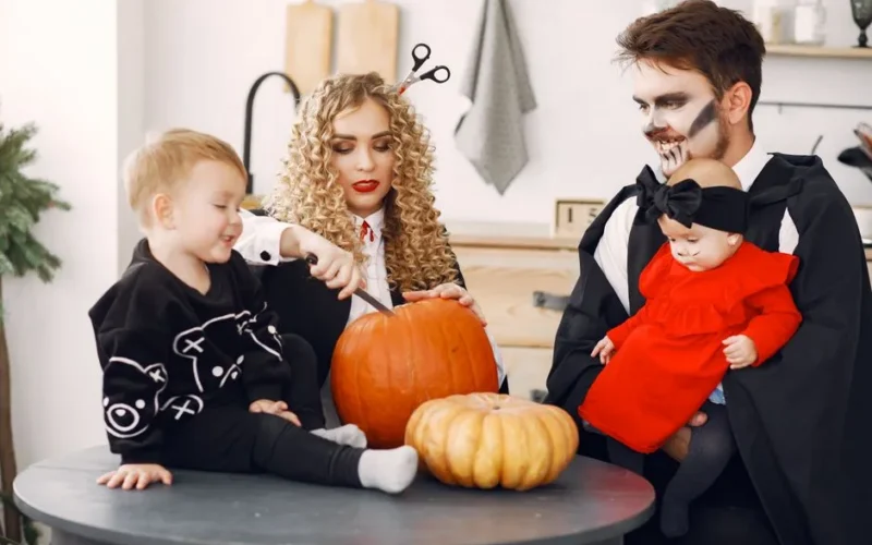 A family in costumes enjoying Halloween with pumpkins in a festive indoor setting.