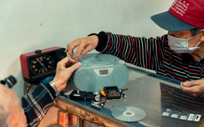 Elderly man repairing a personal stereo in a workshop, showcasing self-employment skills.