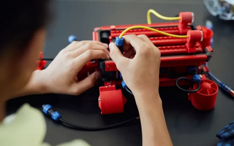 Close-up of hands assembling a robotic project with cables indoors, showcasing technology and electronics.