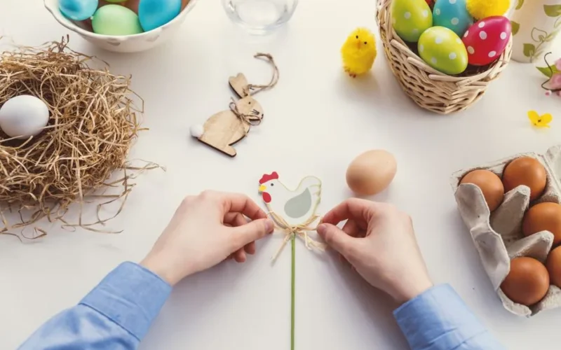 Hands arranging Easter decorations on a table with colorful eggs and festive decor.